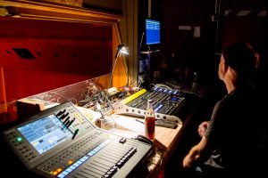 Lichtsteuerpult mit verschiedenen Reglern und Monitoren in einem Veranstaltungsraum.