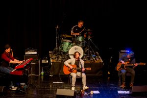 Eine Live-Musikband mit einem Sänger, der Gitarre spielt, und drei weiteren Musikern am Keyboard, Schlagzeug und Bass.